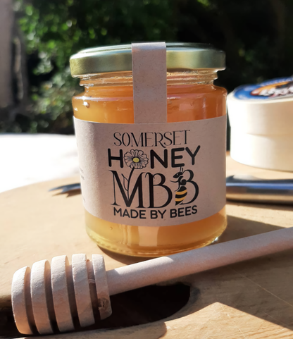 Jar of Somerset Honey with a honey dipper on a wooden surface outdoors