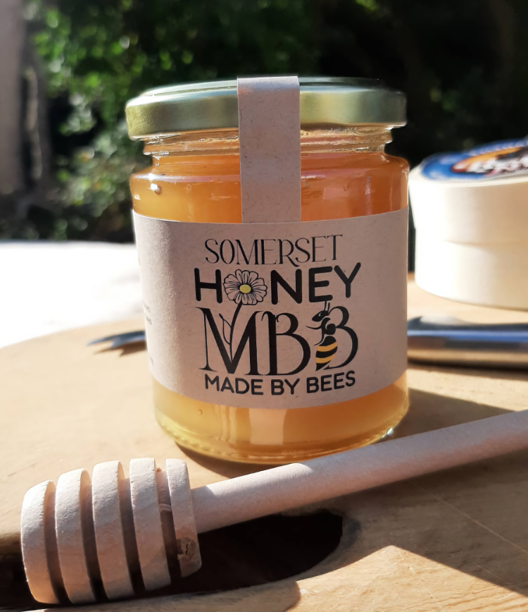 Jar of Somerset Honey with a honey dipper on a wooden surface outdoors